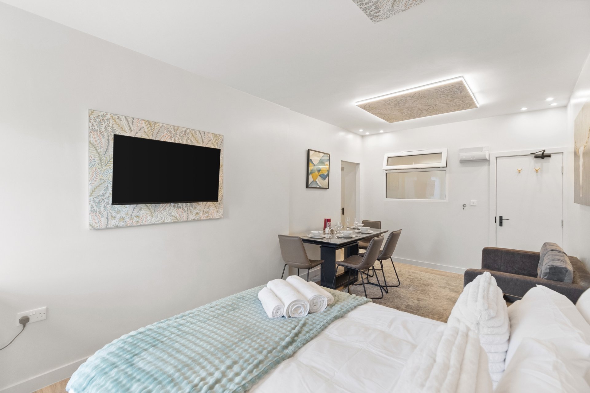Modern studio bedroom with double bed, wall-mounted TV, dining table and chairs