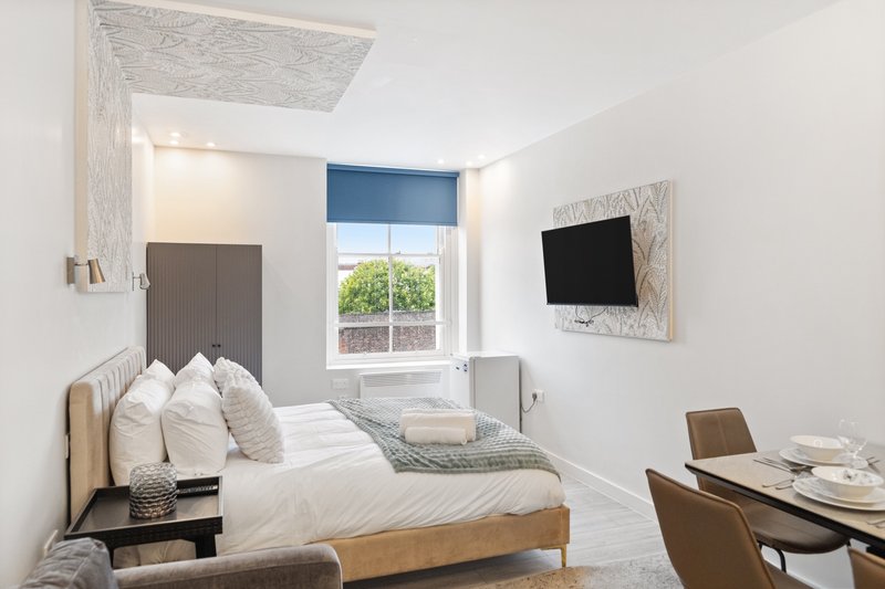 Bright modern bedroom with double bed, wall-mounted TV, desk area and window with blue blind