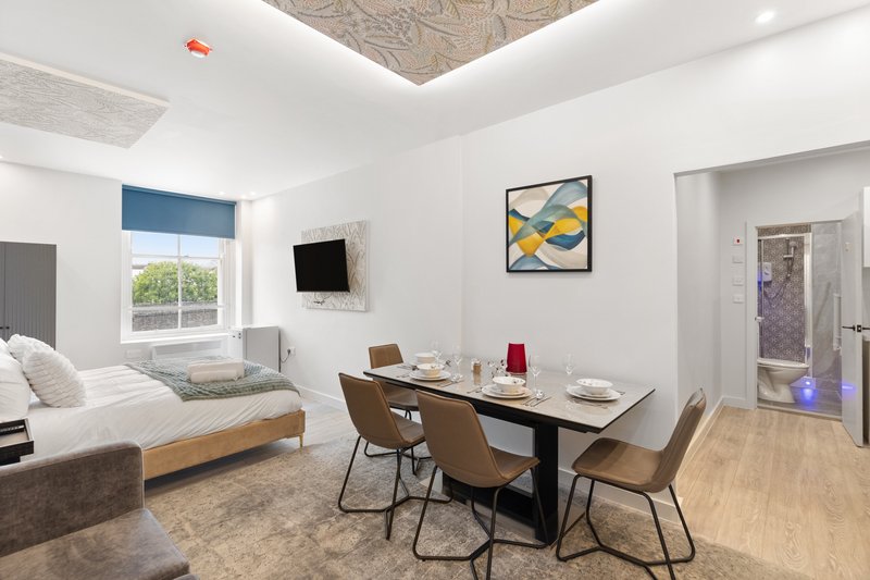 Modern bedroom studio with bed, desk, dining table, and framed wall art