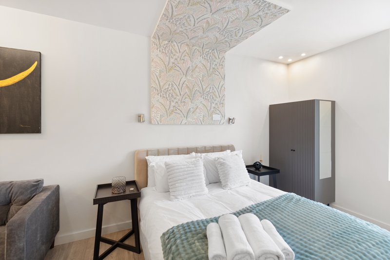 Modern bedroom with double bed, white bedding, dark wardrobe and patterned ceiling feature