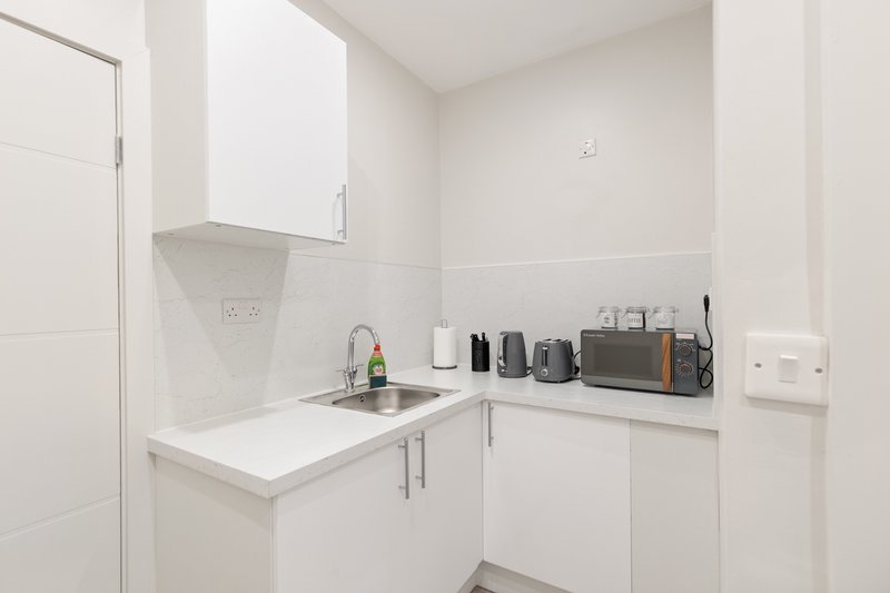 Compact white kitchen with sink, countertop appliances, and wall-mounted cabinets