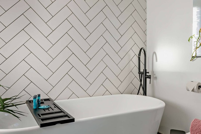 Modern bathroom with freestanding white bathtub, herringbone tile wall, and black faucet