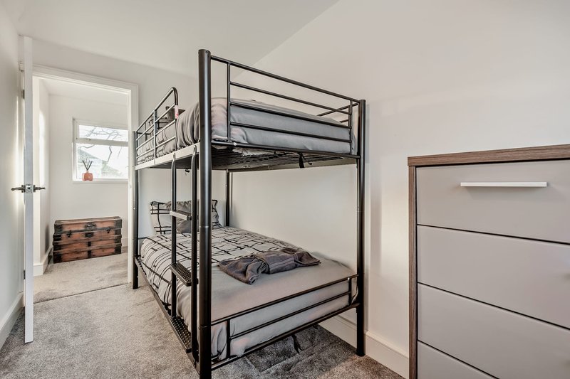 Bedroom with metal bunk bed, wooden chest, dresser and window with natural light