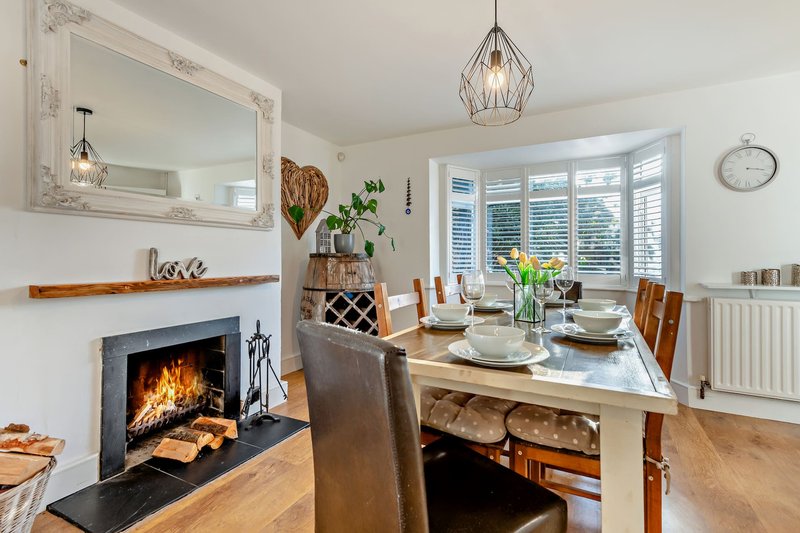 Modern dining room with fireplace, wooden table, chairs, mirror, plants and pendant lighting