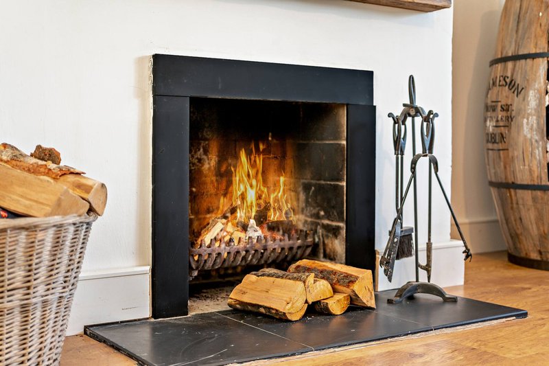 Fireplace with black frame, lit fire, logs, and fireplace tools on wooden floor