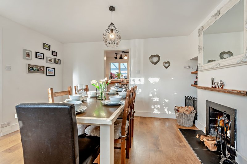 Open-plan dining and kitchen area with wooden table, chairs, fireplace, and pendant lighting