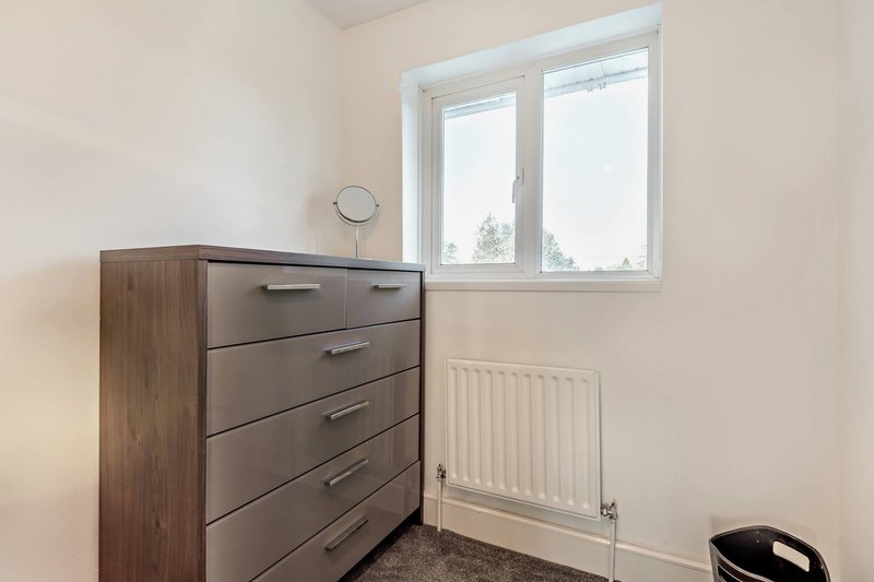 Bright bedroom with wooden chest of drawers, radiator, and large window with natural light