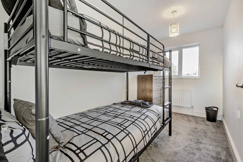Bedroom with metal bunk beds, plaid bedding, window and grey carpet flooring