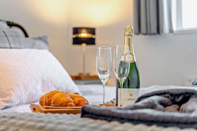 Bedroom with champagne bottle, glasses, croissants on bed with pillows and throws