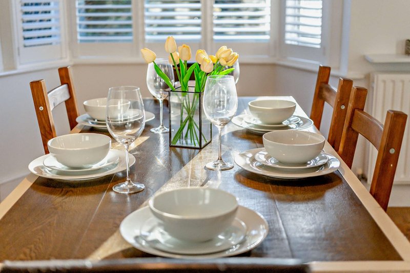 Dining table set for four with white place settings, glasses, and yellow tulips centerpiece