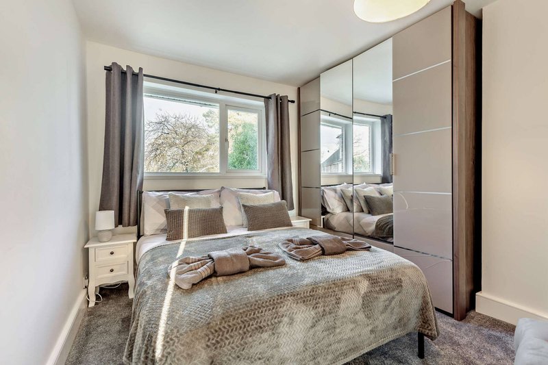 Modern bedroom with double bed, mirrored wardrobe, bedside table and window view