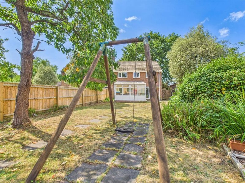 Residential backyard with wooden swing frame, mature trees, and brick house visible in background