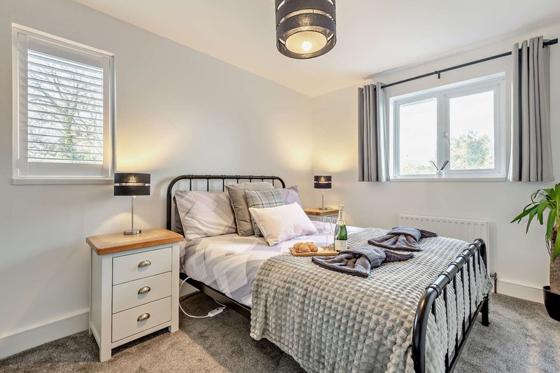 Bright bedroom with double bed, bedside tables, lamps, windows and potted plant