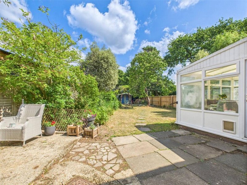 Garden view with patio seating, lush trees, and white garden room building