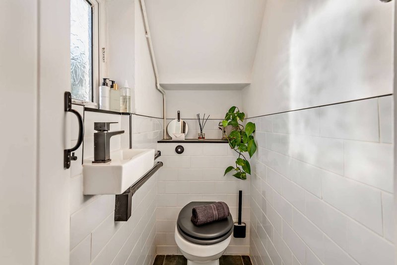 Clean bathroom with white subway tile walls, sink, toilet, and small potted plant