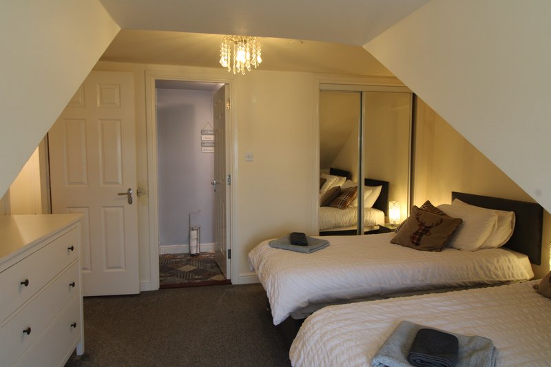 Attic bedroom with two single beds, built-in wardrobe, chest of drawers, and sloped ceiling