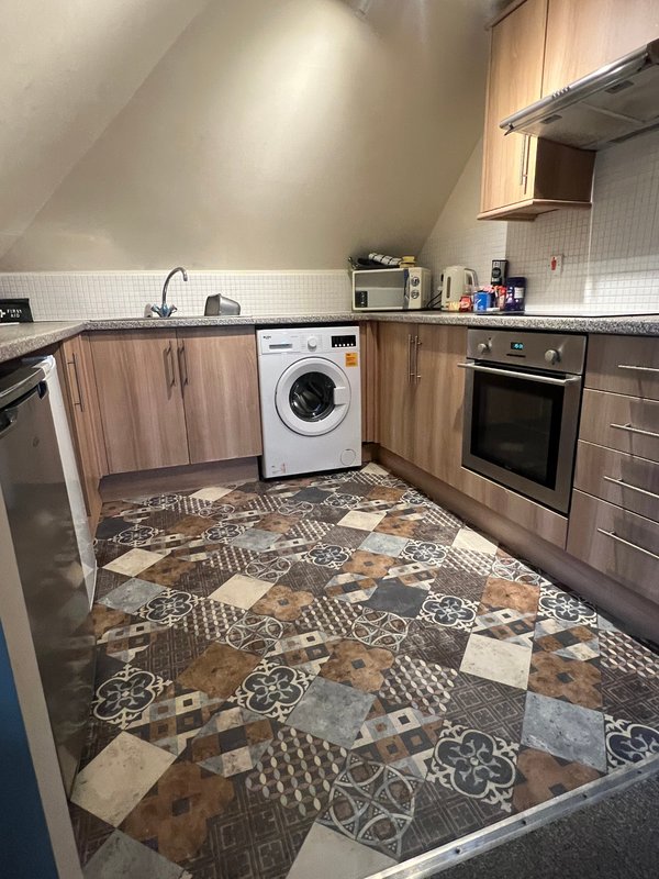 Modern kitchen with wooden cabinets, white washing machine, patterned tile flooring and integrated appliances