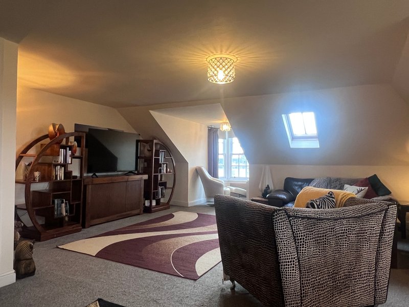 Attic living room with woven armchair, wooden furniture, patterned rug and skylight window
