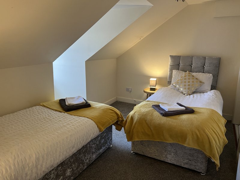 Twin bedroom with sloped ceiling, two single beds with yellow throws, and bedside lamps