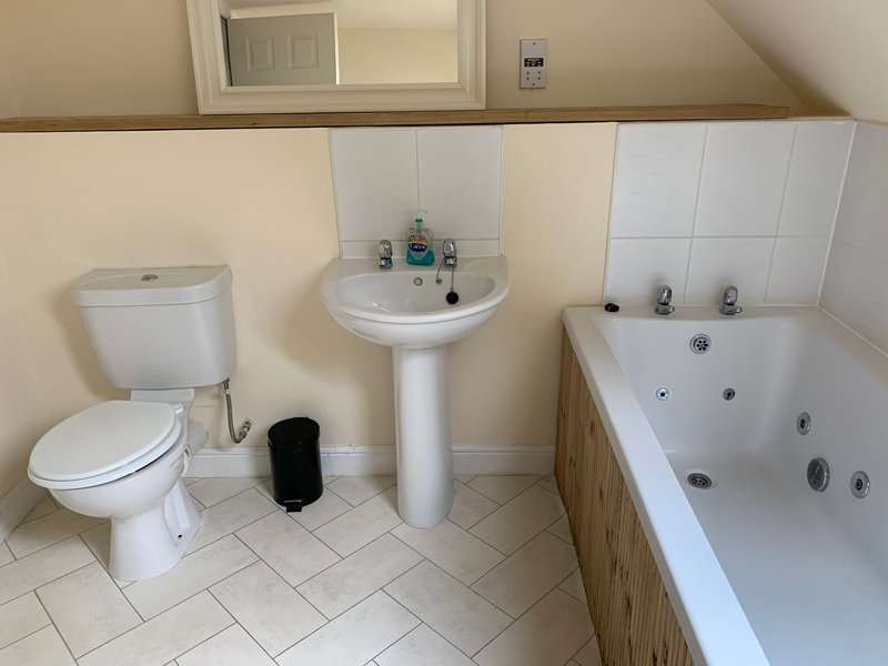Bathroom with toilet, pedestal sink, bathtub with jets, and white tile walls