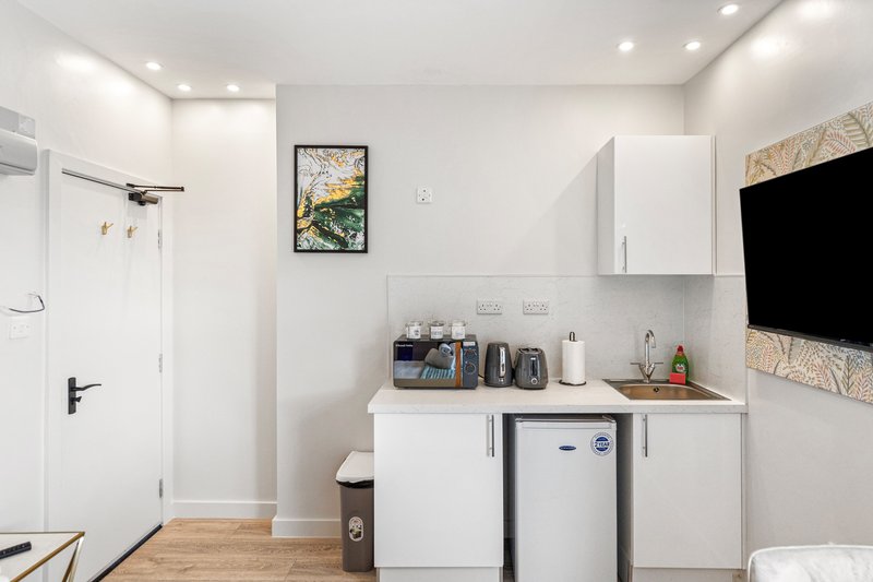 Modern kitchenette with white cabinetry, compact appliances, and framed artwork on wall