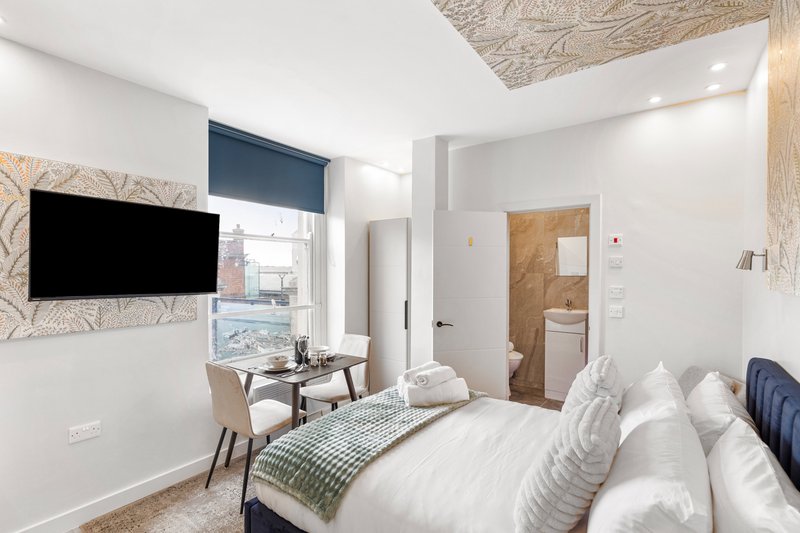 Modern bedroom with double bed, wall-mounted TV, desk area, and en-suite bathroom