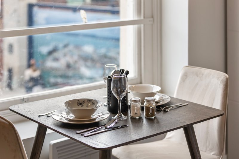 Dining table set for two with champagne bottle, glasses, and place settings near window