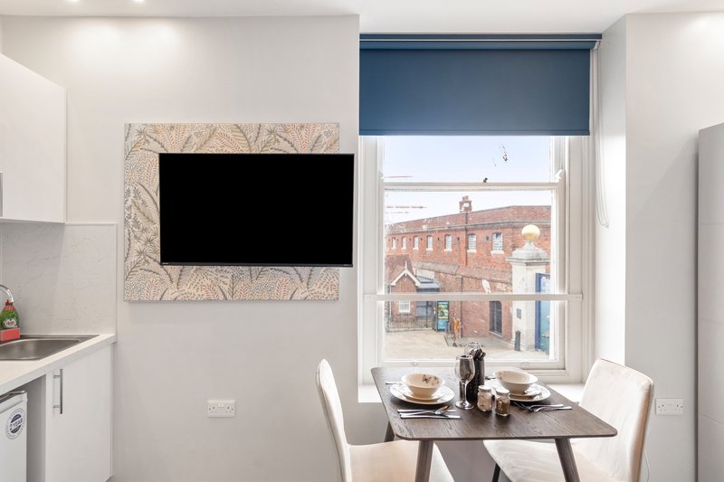 Modern kitchen-diner with wall-mounted TV, dining table, window overlooking brick buildings
