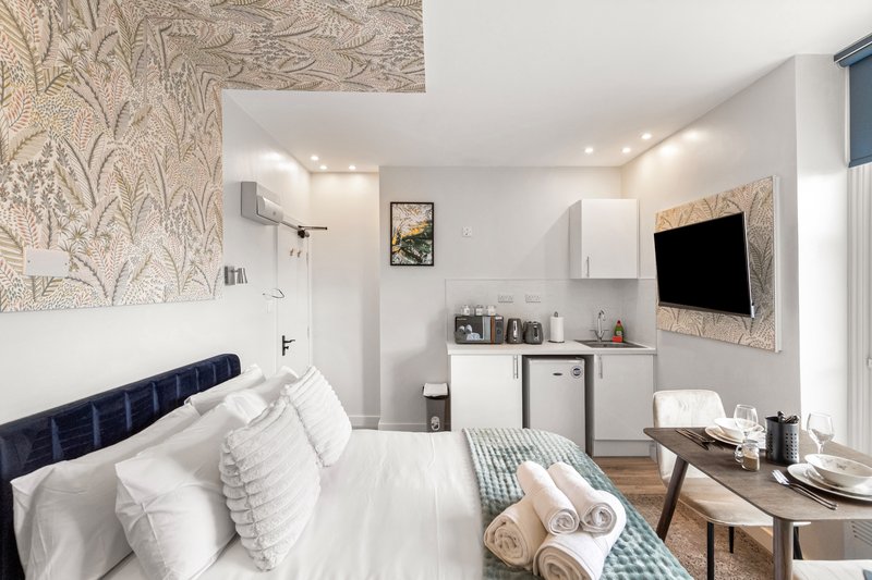 Modern bedroom with double bed, white pillows, wall-mounted TV, desk area and patterned wallpaper
