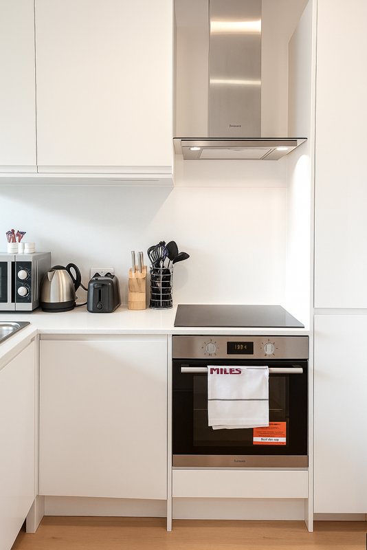 Modern white kitchen with built-in oven, hob, and stainless steel extractor hood