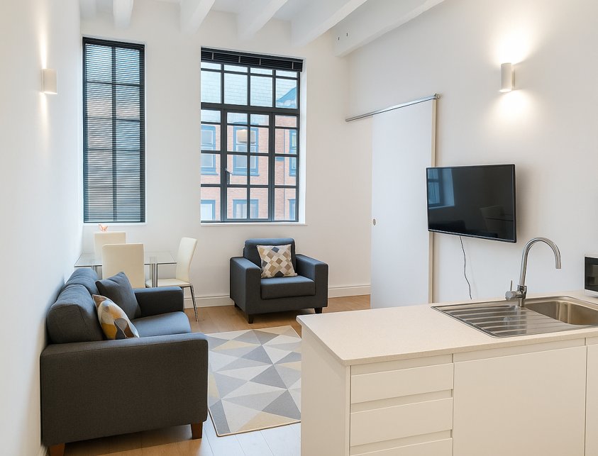 Open-plan studio with black sofa, armchair, kitchenette, wall-mounted TV and large windows