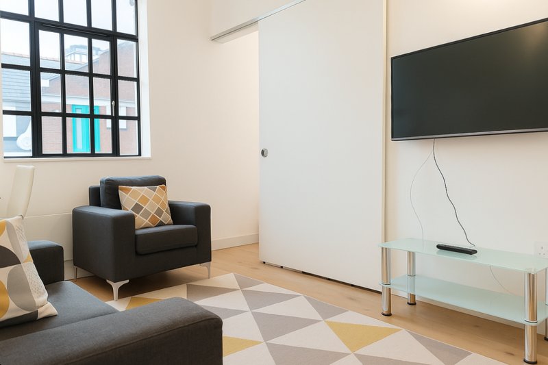 Modern living room with black armchair, gray sofa, geometric rug and wall-mounted TV