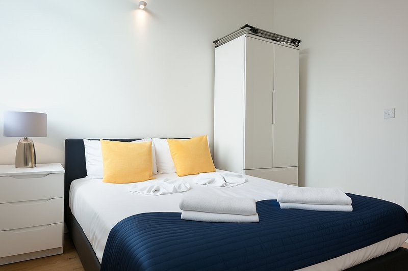Modern bedroom with double bed, yellow cushions, navy bedding, and white wardrobe