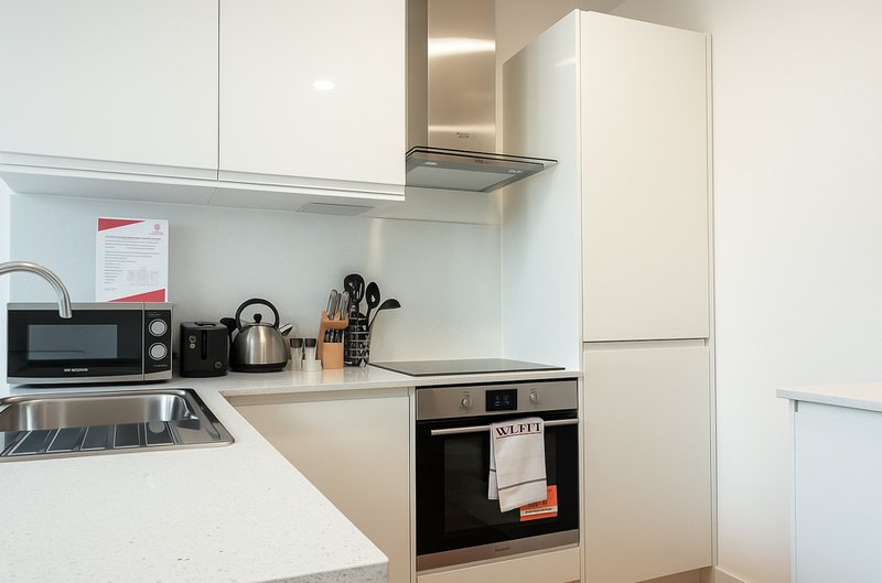 Modern white kitchen with built-in oven, microwave, kettle and cooking utensils on countertop