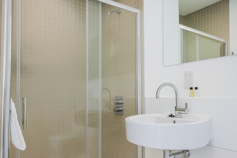 Modern bathroom with curved white sink, chrome faucet, glass shower enclosure and mirrored cabinet