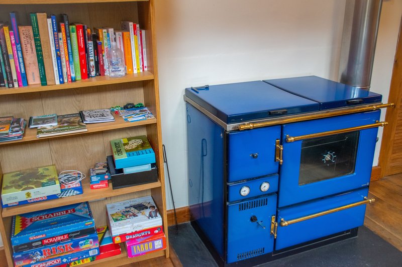 Living room with wooden bookshelf displaying books and board games, blue Aga-style cooker, wooden floor
