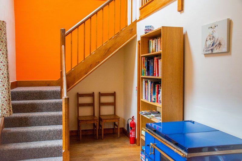 Staircase with orange wall, wooden steps, bookshelf, chairs and blue table