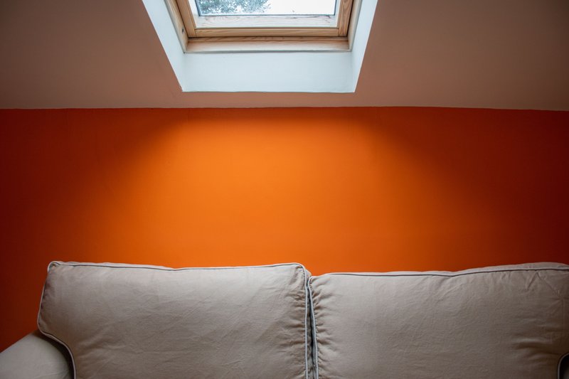 Bright attic bedroom with beige sofa, orange accent wall, and skylight window