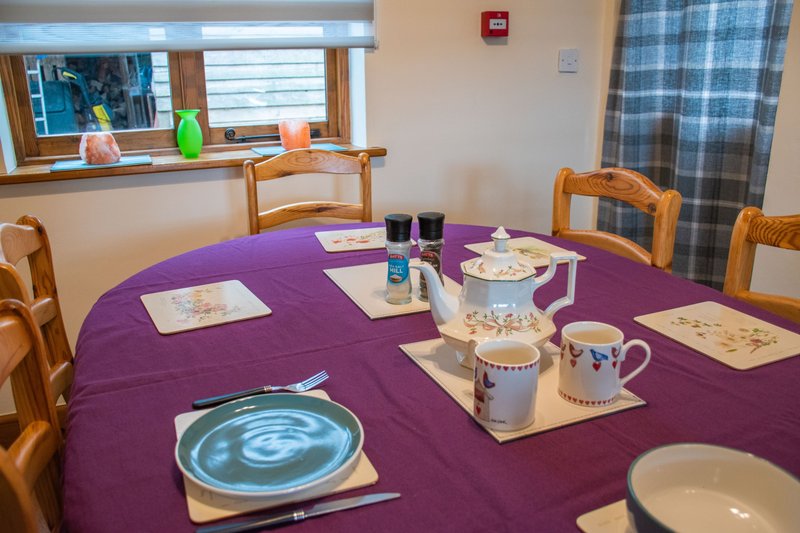 Dining room with purple tablecloth, wooden chairs, place settings and tableware