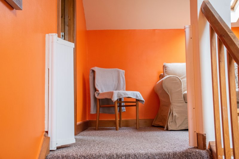 Bright orange bedroom with wooden beams, chair with towel, and carpeted floor