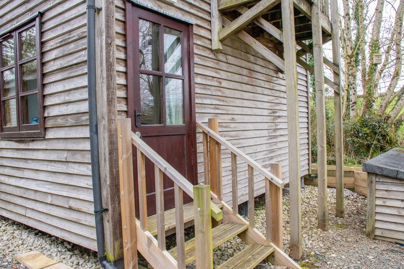 Exterior view of wooden cabin with red door, wooden ramp, and gravel ground