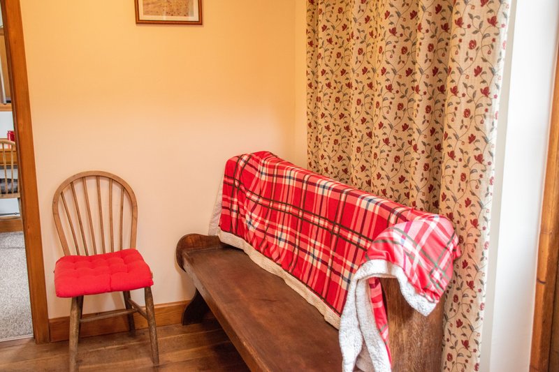 Bedroom corner with wooden chair, bench, red plaid blanket, and floral curtains