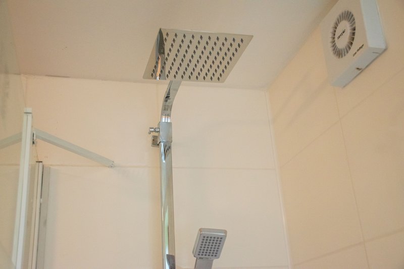 Modern bathroom with rainfall showerhead, tile walls, and ventilation unit mounted on ceiling