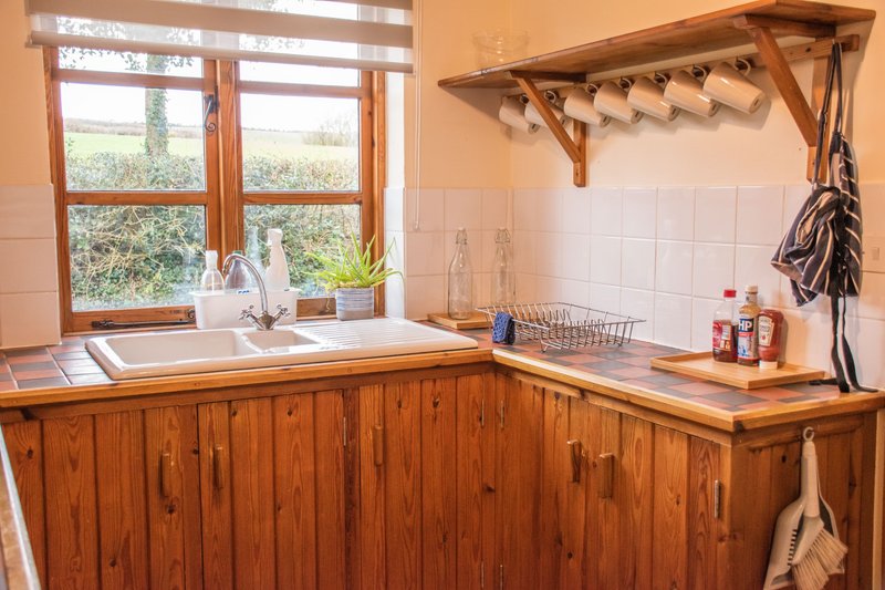 Rustic kitchen with wooden cabinetry, sink, window view, and hanging utensils