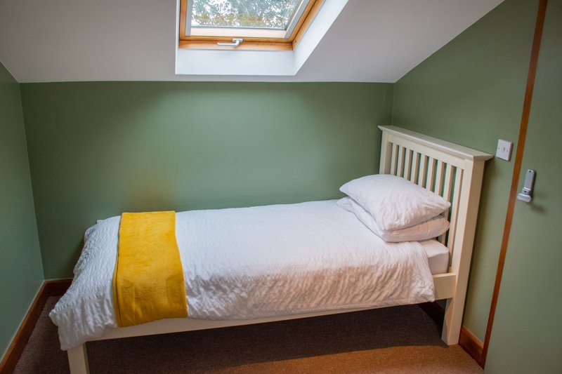 Bedroom with single bed, white headboard, green walls and skylight window
