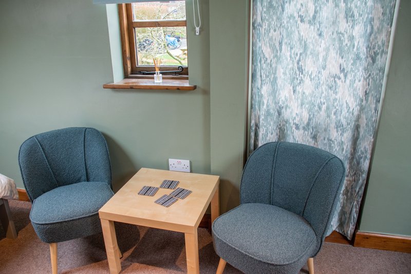 Seating area with two blue upholstered chairs, wooden table, window and curtains