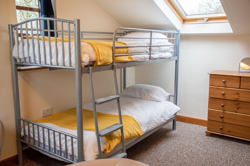 Attic bedroom with metal bunk beds, yellow bedding, wooden chest of drawers and skylight