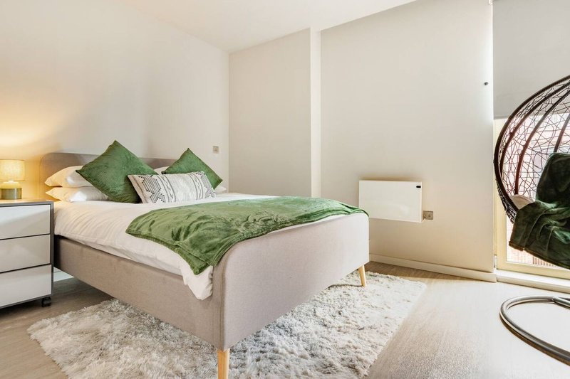 Modern bedroom with double bed, green bedding, white nightstands and pendant chair in corner