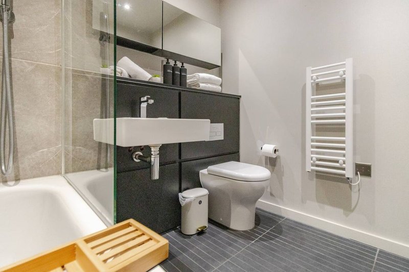 Modern bathroom with shower enclosure, white sink, toilet, heated towel rail and wooden mat
