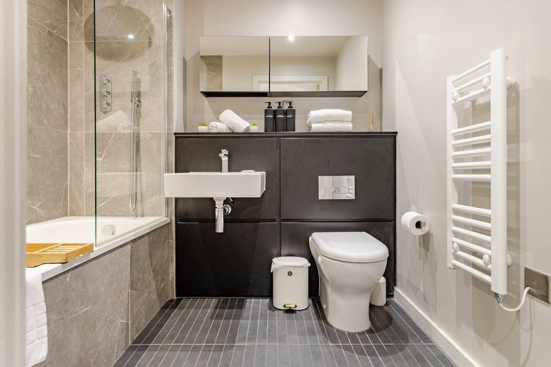 Modern bathroom with black vanity, white sink, toilet, shower enclosure and heated towel rail
